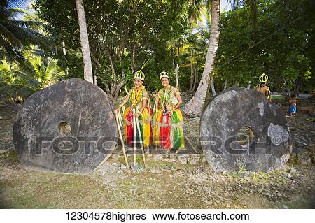 Stock Photograph - These two young girls between the two pieces of stone money, are in a traditional outfit for cultural ceremonies on the island of Yap; Yap, Federated States of Micronesia. Fotosearch