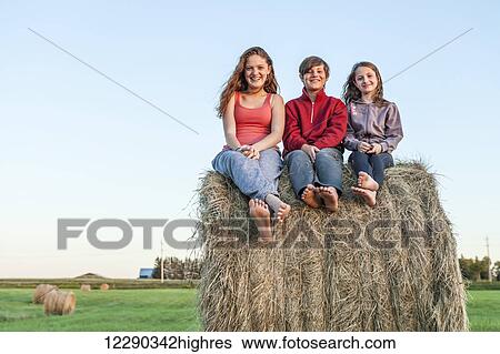 Stock Photograph - Three kids sitting on hay bale; Ontario, Canada. Fotosearch