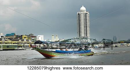 Stock Photograph - Tour boat in the river with a skyscraper and bridge in the background; Bangkok, Thailand. Fotosearch