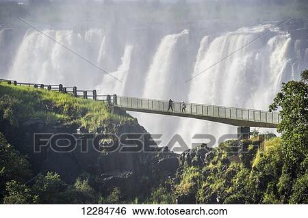 Stock Photograph - Tourist walkway across cliff edge at Victoria Falls waterfall; Livingstone, Zambia. Fotosearch
