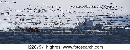 Stock Photograph - Tourists on an inflatable boat and a ship in the water; Spitsbergen, Svalbard, Norway. Fotosearch