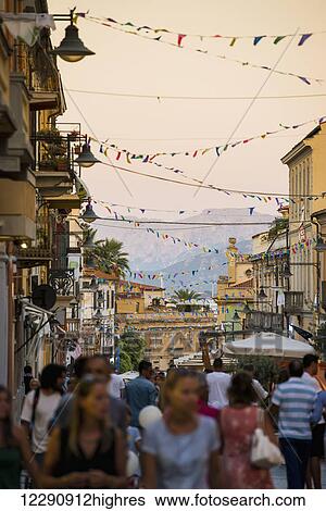Stock Photograph - Tourists walking down a busy street at dusk; Olbia, Sardinia, Italy. Fotosearch