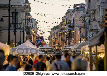 Stock Photograph - Tourists walking down a busy street at dusk; Olbia, Sardinia, Italy. Fotosearch