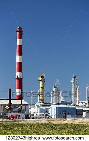 Stock Photograph - Towers of a gas plant with a red and white striped large stack with blue sky; Crossfield, Alberta, Canada. Fotosearch