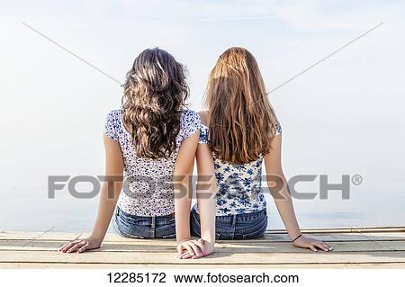 Two girls holding hands sitting close together at end of a dock; Toronto, Ontario, Canada View Large Photo Image Stock Image - Two girls holding hands sitting close together at end of a dock; Toronto, Ontario, Canada. Fotosearch