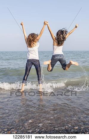 Stock Image - Two girls jumping in the water at beach; Toronto, Ontario, Canada. Fotosearch