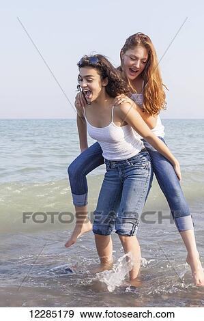 Stock Photo - Two girls playing piggyback at beach; Toronto, Ontario, Canada. Fotosearch