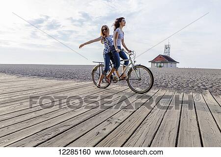 Two girls riding double on a single bike on a beach boardwalk; Toronto, Ontario, Canada View Large Photo Image Stock Image - Two girls riding double on a single bike on a beach boardwalk; Toronto, Ontario, Canada. Fotosearch
