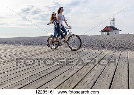 Two girls riding double on a single bike on a beach boardwalk; Toronto, Ontario, Canada View Large Photo Image Stock Image - Two girls riding double on a single bike on a beach boardwalk; Toronto, Ontario, Canada. Fotosearch