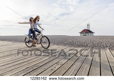 Two girls riding double on a single bike on a beach boardwalk; Toronto, Ontario, Canada View Large Photo Image Stock Image - Two girls riding double on a single bike on a beach boardwalk; Toronto, Ontario, Canada. Fotosearch