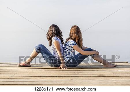 Two girls sitting back-to-back at end of a dock; Toronto, Ontario, Canada View Large Photo Image Stock Image - Two girls sitting back-to-back at end of a dock; Toronto, Ontario, Canada. Fotosearch