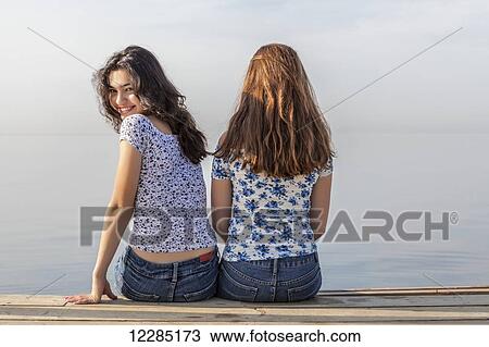 Two girls sitting close together at end of a dock; Toronto, Ontario, Canada View Large Photo Image Stock Image - Two girls sitting close together at end of a dock; Toronto, Ontario, Canada. Fotosearch