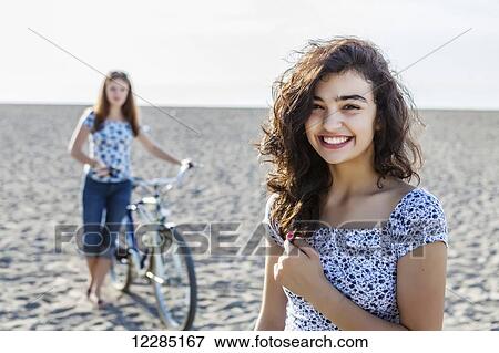 Stock Photo - Two girls standing on a beach with bike; Toronto, Ontario, Canada. Fotosearch