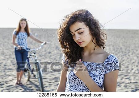 Stock Photography - Two girls standing on a beach with bike; Toronto, Ontario, Canada. Fotosearch