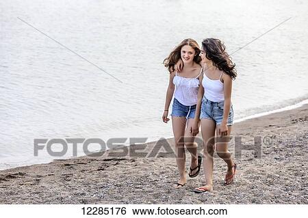 Stock Photograph - Two girls walking along shoreline at beach; Toronto, Ontario, Canada. Fotosearch