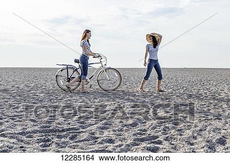 Two girls walking on beach with bike; Toronto, Ontario, Canada View Large Photo Image Picture - Two girls walking on beach with bike; Toronto, Ontario, Canada. Fotosearch