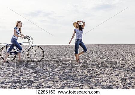 Stock Image - Two girls walking on beach with bike; Toronto, Ontario, Canada. Fotosearch
