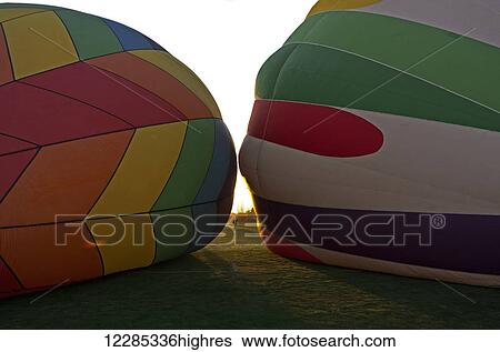 Stock Photograph - Two hot air balloons lying on ground, tops facing each other, girl taking photo seen between them in the distance; Ripon, California, United States of America. Fotosearch