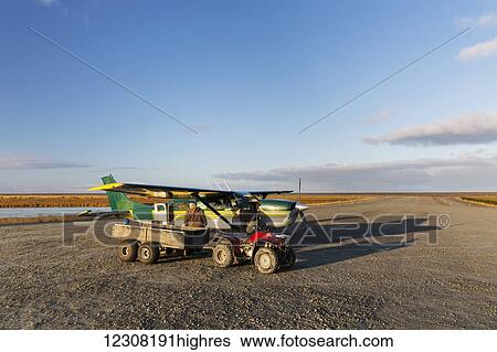 Stock Photograph - Two Men unload cargo into a four wheeler beside a bush plane on an remote airstrip in Alakanuk, Yukon Delta, Arctic Alaska, USA, Fall. Fotosearch