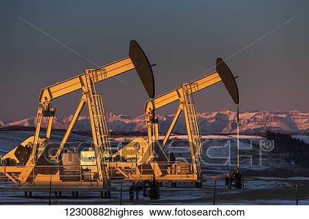 Two pump jacks at sunrise reflecting the warm morning light in a snow covered field and snow covered foothills and mountains in the background lit by the morning sun; Alberta, Canada View Large Photo Image Stock Photograph - Two pump jacks at sunrise reflecting the warm morning light in a snow covered field and snow covered foothills and mountains in the background lit by the morning sun; Alberta, Canada. Fotosearch