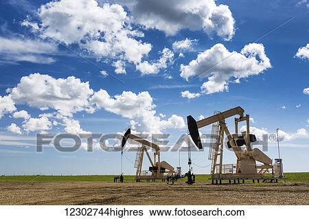 Stock Photograph - Two pump jacks in a field with large puffy clouds and blue sky; Alberta, Canada. Fotosearch