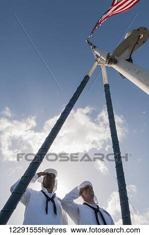 Stock Photograph - Two sailors in dress white uniform salute the flag on a ship as it moors in port; Hawaii, United States of America. Fotosearch