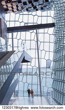 Two tourists explore the Harpa Public Concert Hall, designed by the Danish firm Henning Larsen Architects and the Icelandic firm Batteriao Architects, the glass facade designed by Icelandic glass artist Olafur Eliasson; Reykjavik, Iceland View Large Photo Image Stock Photograph - Two tourists explore the Harpa Public Concert Hall, designed by the Danish firm Henning Larsen Architects and the Icelandic firm Batteriao Architects, the glass facade designed by Icelandic glass artist Olafur Eliasson; Reykjavik, Iceland. Fotosearch