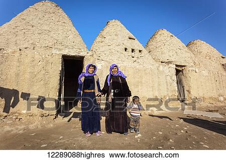 Stock Photograph - Two women and a child standing outside the doorway of a primitive dwelling; Harran, Turkey. Fotosearch