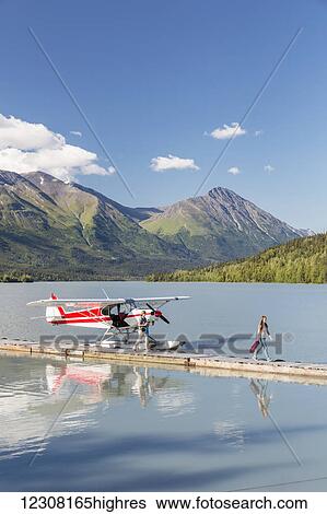 Stock Photograph - Two women disembark from a float plane docked at the Trail Lake Float Plane Base on a clear day, the Kenai Mountains in the Background, Kenai Peninsula, Southcentral Alaska, USA, Summer. Fotosearch