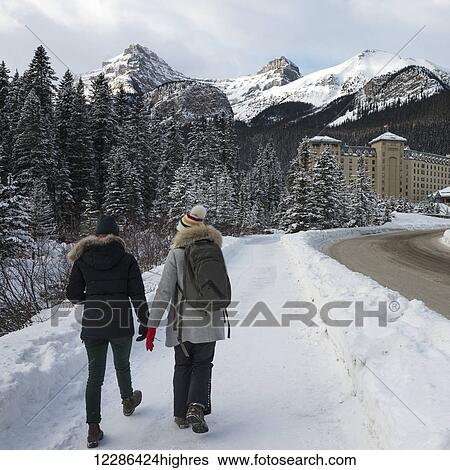 Stock Photograph - Two young women walking on a snowy trail towards Chateau Lake Louise; Lake Louise, Alberta, Canada. Fotosearch