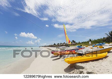 View looking down the white sand beach on a sunny day with kayaks and boats resting in the sand and people in the ocean in the distance; Varadero, Cuba View Large Photo Image Stock Photograph - View looking down the white sand beach on a sunny day with kayaks and boats resting in the sand and people in the ocean in the distance; Varadero, Cuba. Fotosearch