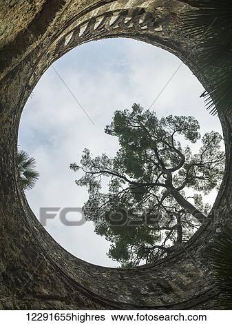 Stock Photograph - View looking up through a circular opening to a cloudy sky and tree; Ravello, Italy. Fotosearch