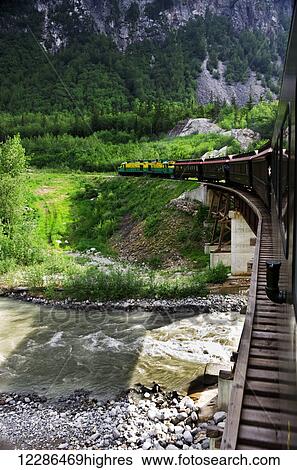 Stock Photograph - White Pass Railroad electric engine pulls train passenger cars over trestle bridge, Skagway, Southeast Alaska. Fotosearch