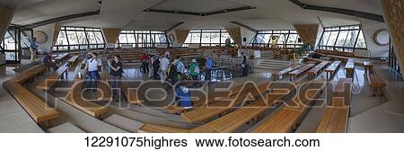 Stock Photograph - Wide angle view of tourists in a room with wooden benches and big windows, a site believed to be the ruins of Peter's house; Capernaum, Israel. Fotosearch