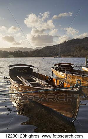 Stock Photograph - Woden boats tied at the water's edge on a tranquil lake; South Lakeland District, England. Fotosearch