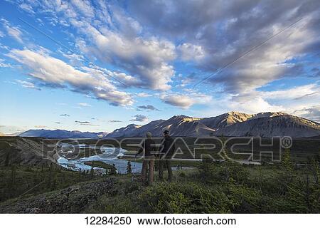 Stock Image - Woman and man looking out at the Wind River in the Peel Watershed; Yukon, Canada. Fotosearch