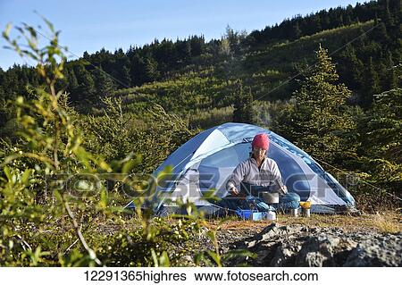 Stock Photograph - Woman backpacker prepares a meal at camp near Upper Fuller Lake in the Kenai National Wildlife Refuge on the Kenai Peninsula in South-central Alaska. Fotosearch