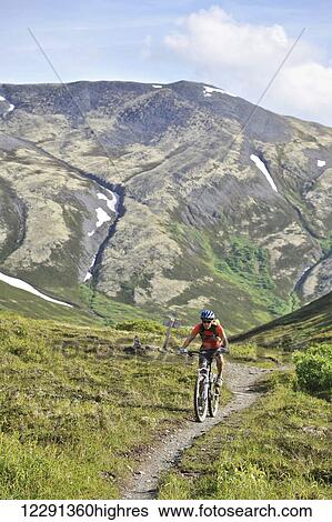 Stock Photograph - Woman rides a full suspension mountain bike on the Resurrection Pass Trail in the Chugach National Forest, Kenai Peninsula, South-central Alaska. Fotosearch