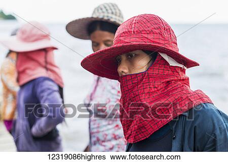 Stock Photograph - Women wearing hats and scarves covering their mouths, local life in the famous Crab Market; Kep, Cambodia. Fotosearch