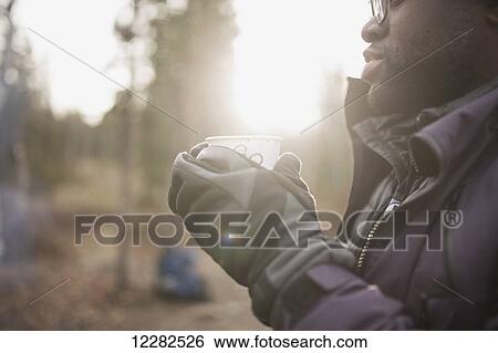 Stock Photograph - Young African-American man holding coffee with gloved hands outside and near the Arctic Circle, Alaska. Fotosearch