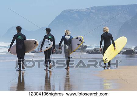 Young male surfers walking on the wet beach towards the water with their surfboards; Praia da Cordoama, Portugal View Large Photo Image Stock Photograph - Young male surfers walking on the wet beach towards the water with their surfboards; Praia da Cordoama, Portugal. Fotosearch