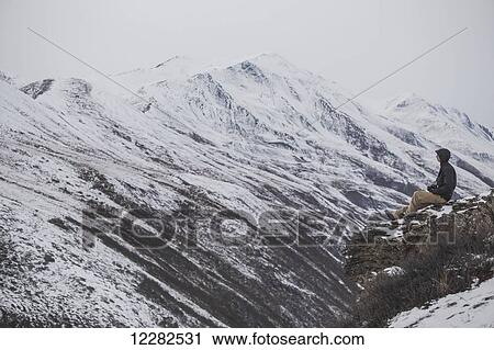 Young man perched on cliff overlooking an arctic valley, Arctic Alaska, late Autumn View Large Photo Image Stock Image - Young man perched on cliff overlooking an arctic valley, Arctic Alaska, late Autumn. Fotosearch