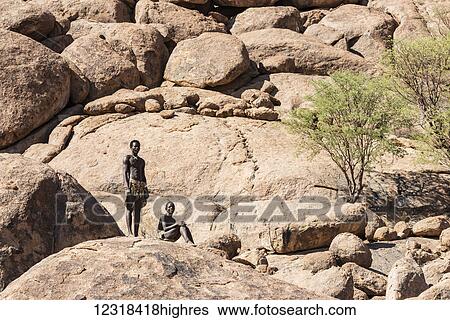 Stock Photograph - Young men in traditional Damara People clothes are posing at the The Living Museum of the Damara on a rocky background; Namibia. Fotosearch