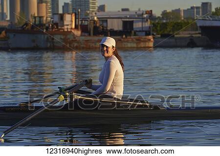 Stock Photograph - Young woman in a single scull, Hanlan Boat Club in the harbour; Toronto, Ontario, Canada. Fotosearch