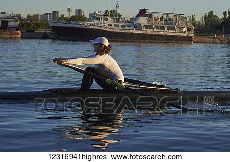 Stock Photograph - Young woman in a single scull, Hanlan Boat Club in the harbour; Toronto, Ontario, Canada. Fotosearch