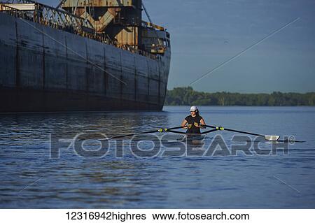 Stock Photograph - Young woman in a single scull, Hanlan Boat Club in the harbour; Toronto, Ontario, Canada. Fotosearch