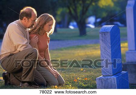 Stock Image - Father and daughter kneeling by graveside. Fotosearch