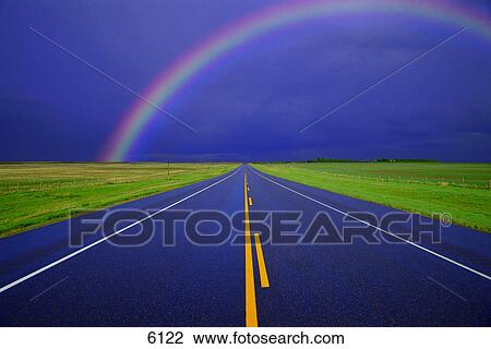 Stock Image - Two-lane road in country on rainy day with rainbow. Fotosearch