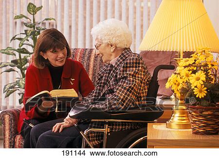 Picture - Woman reading to senior relative on wheelchair. Fotosearch