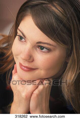 Stock Image - Closeup of young woman's face with chin on hands. Fotosearch